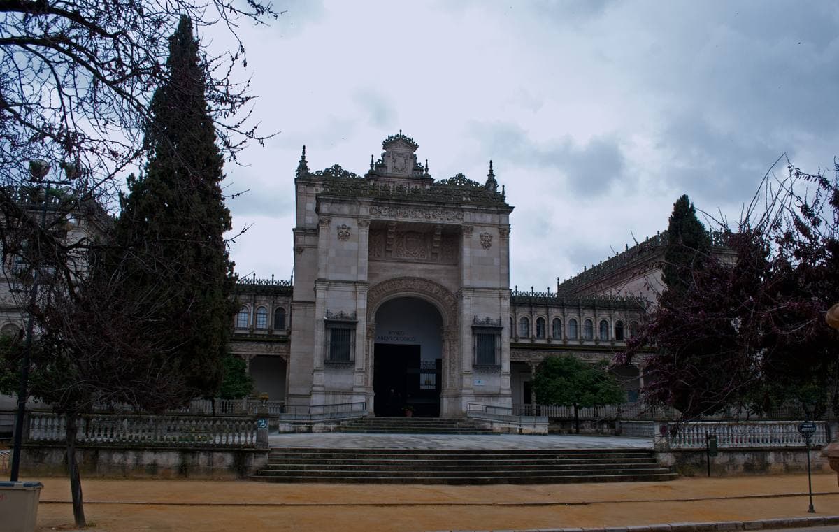 A carved stone pavilion front with a deep arched doorway behind cypress trees