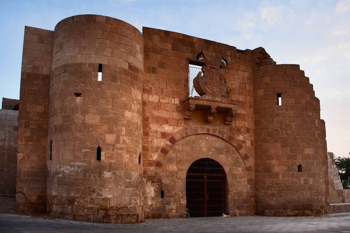 A round stone tower and an arched gateway under a carved coat of arms