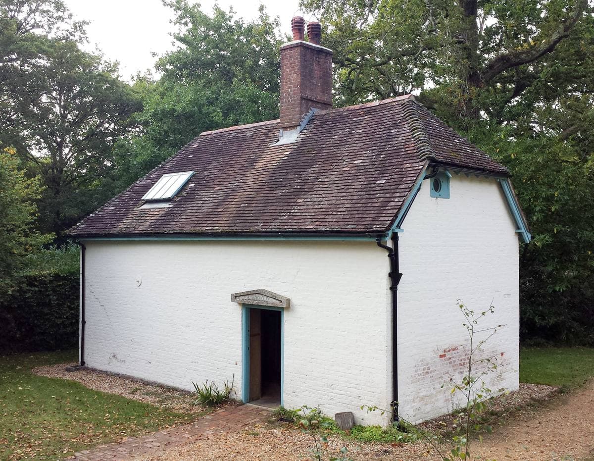 A small white cottage with a brick chimney among trees