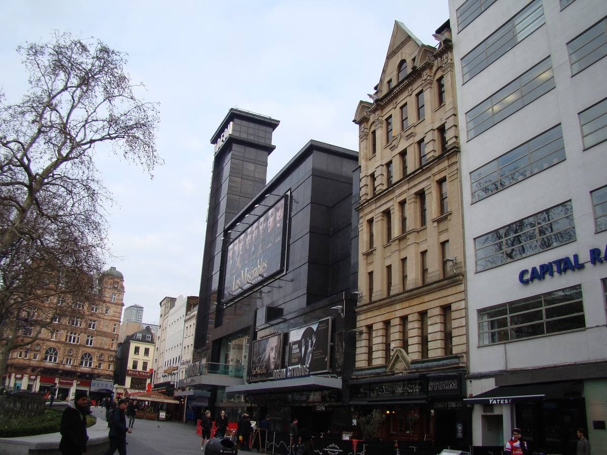 A tall dark cinema tower over Leicester Square with people walking by