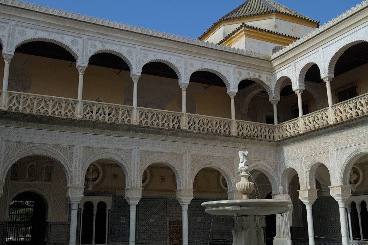 A white arcaded courtyard with a fountain in the middle and statues at the corners