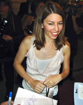 Sofia Coppola, smiling, signing autographs in a pale sleeveless top