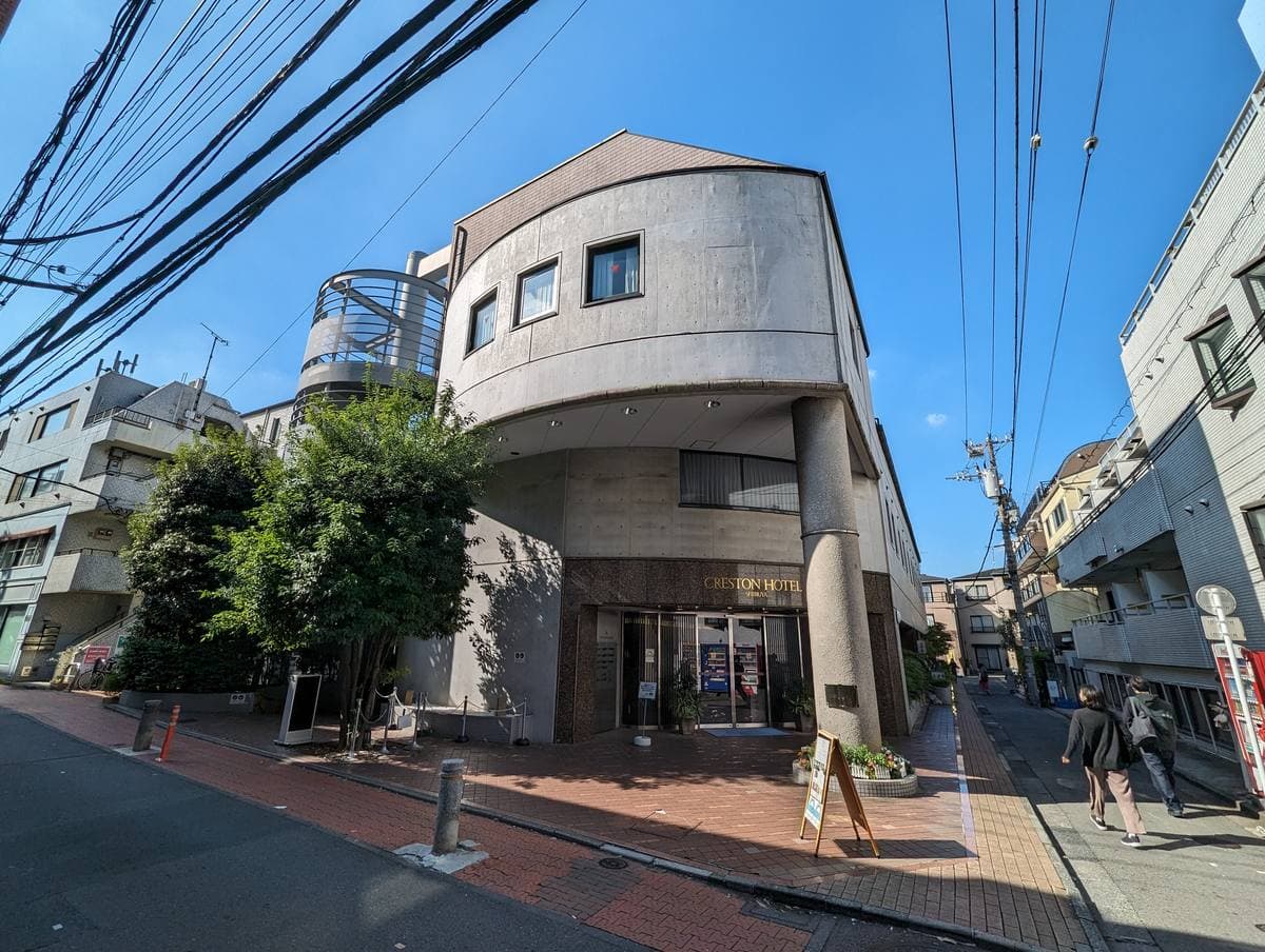 A curved, cream-coloured hotel building on a quiet Shibuya street under a blue sky