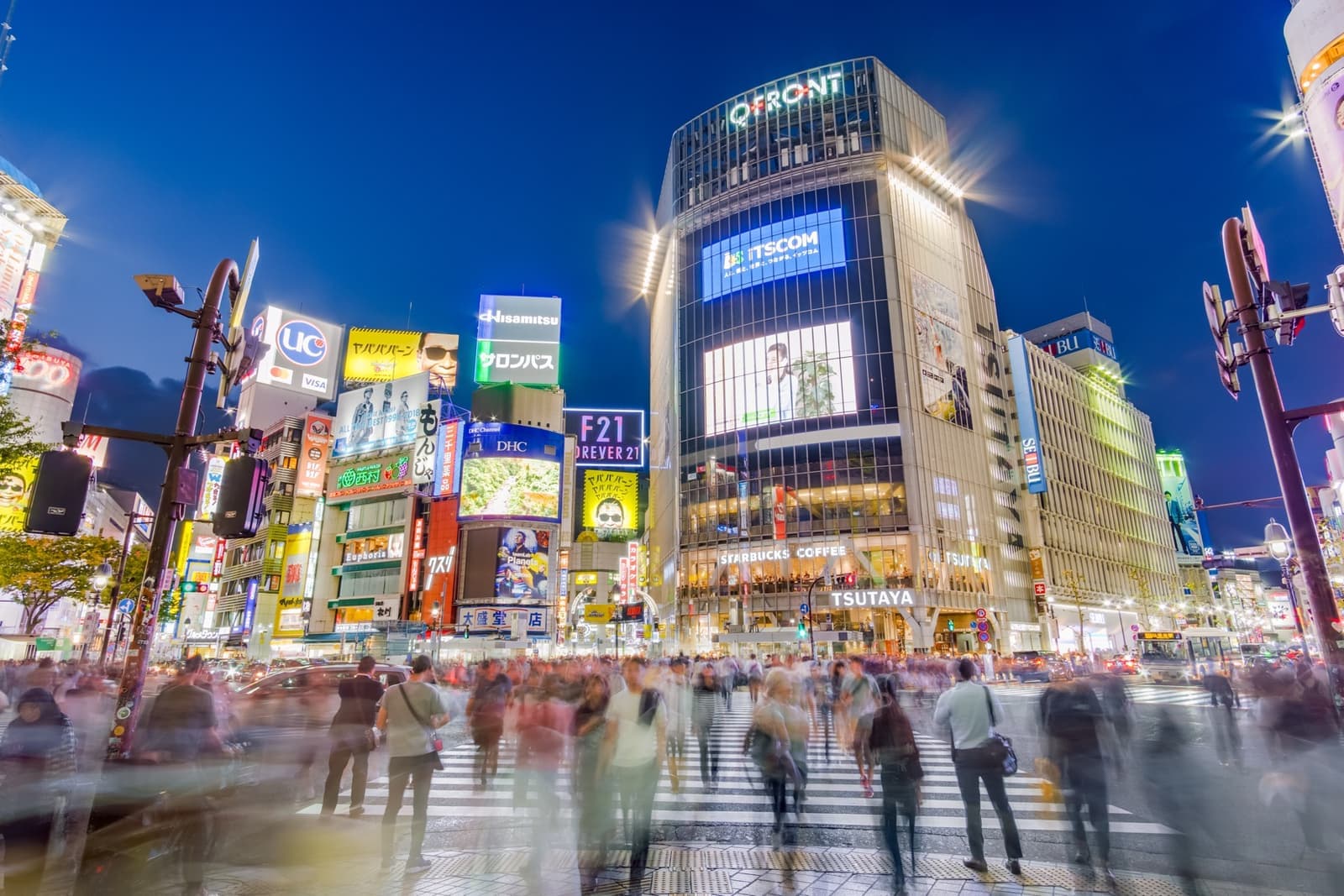 Crowds blurred in motion on the zebra crossings below lit buildings and screens