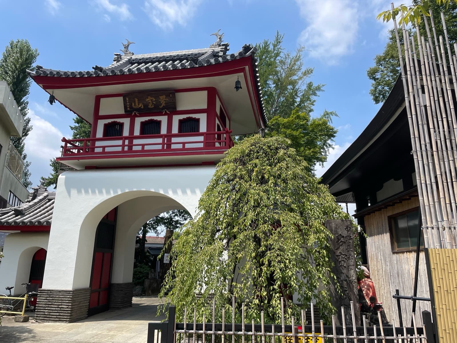 A white-arched temple gate with a red and white upper storey and a weeping tree