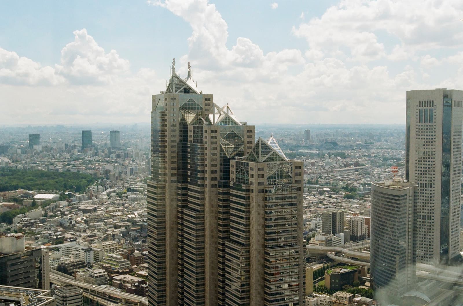 A stepped glass tower with pointed glass roofs above a wide grey city
