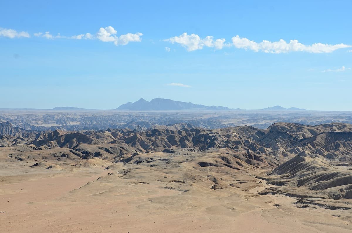 Eroded grey desert ridges with a long dark mountain behind