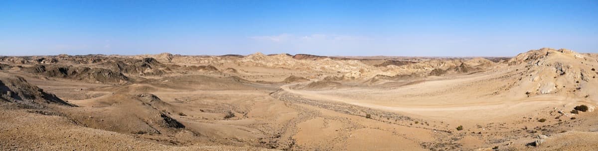 A wide panorama of bare, folded grey-brown desert hills