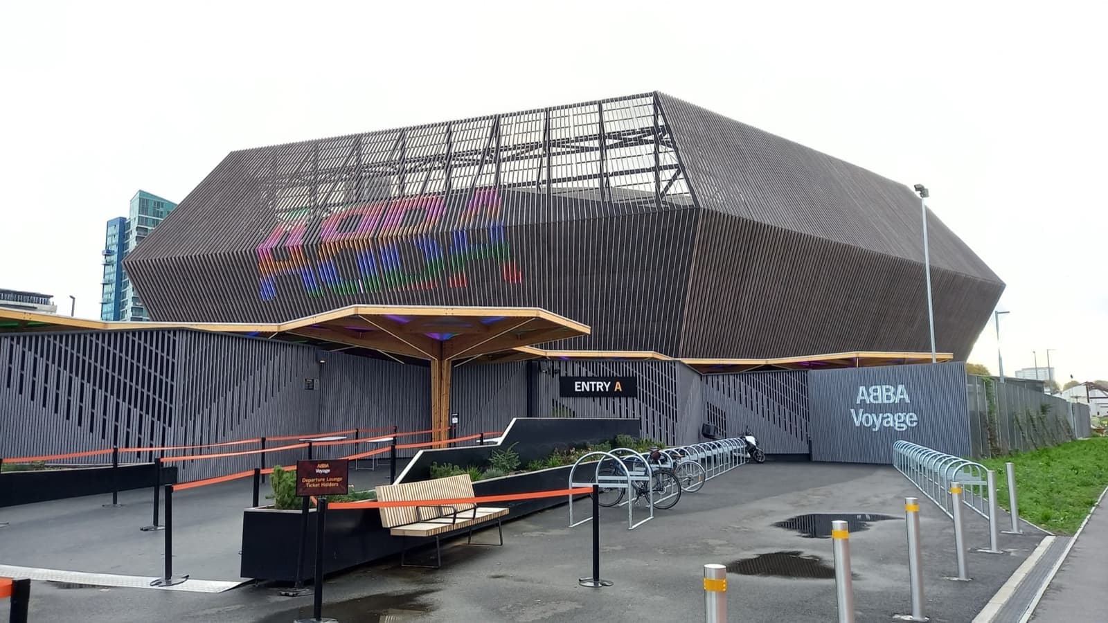 A dark, angular arena building with coloured lettering on its side and a covered entrance