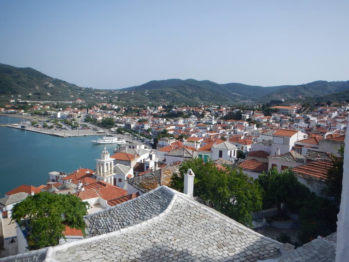 Whitewashed houses and red roofs of Skopelos Town above a blue bay, with green hills behind