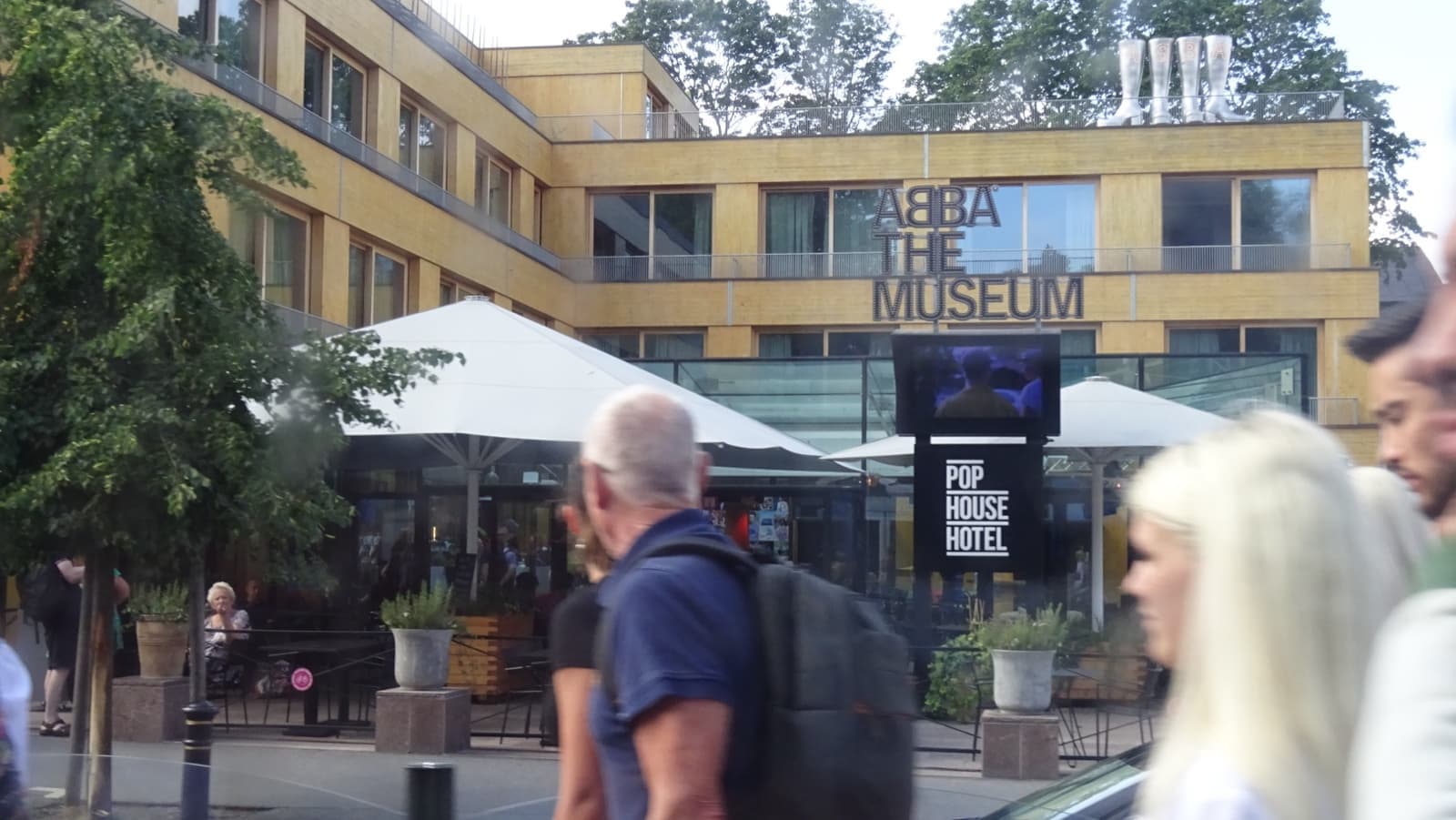 The front of a pale museum building with the words ABBA The Museum, visitors walking past