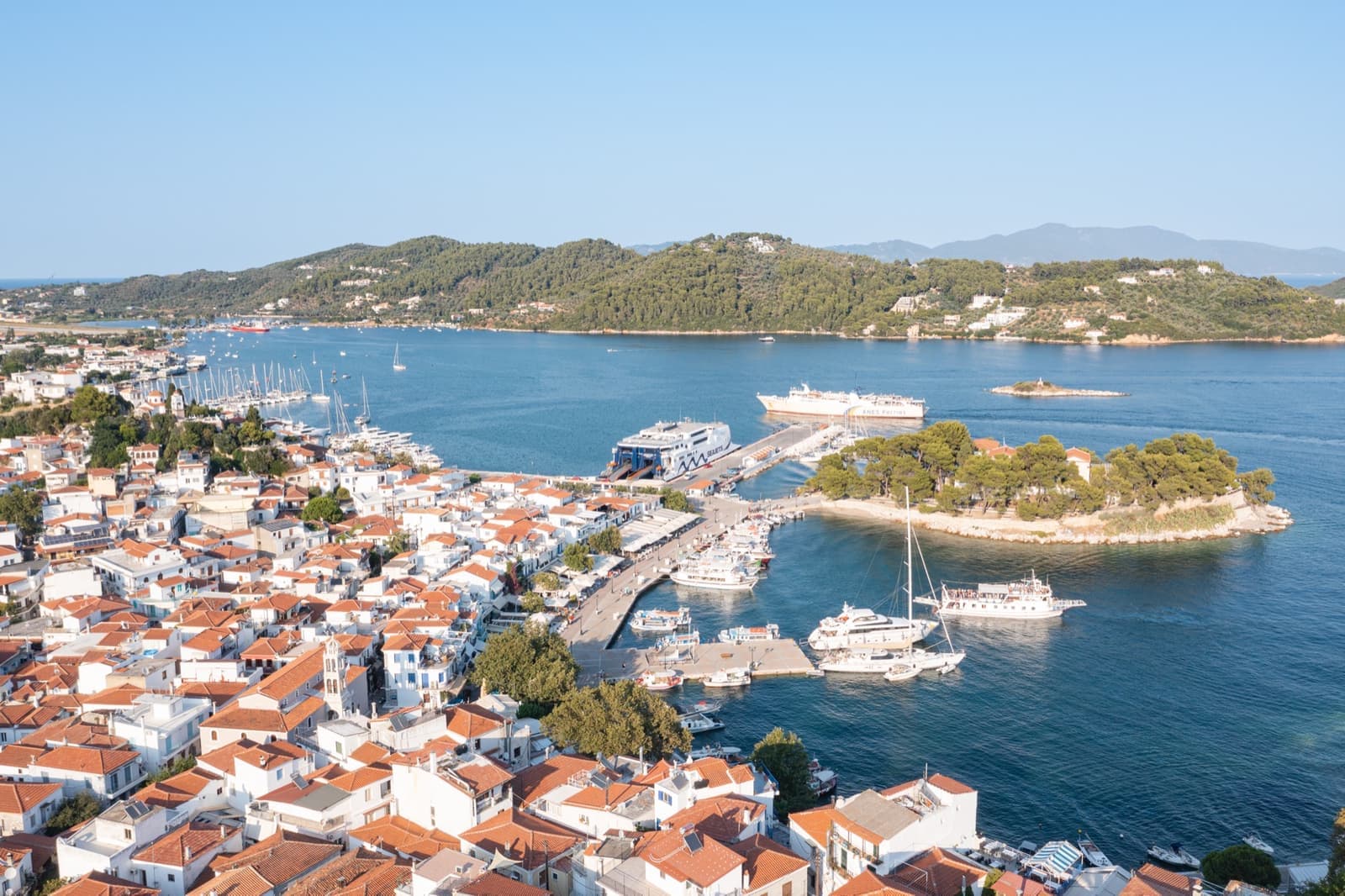 A harbour town with red roofs, a small wooded peninsula and boats moored along the quay