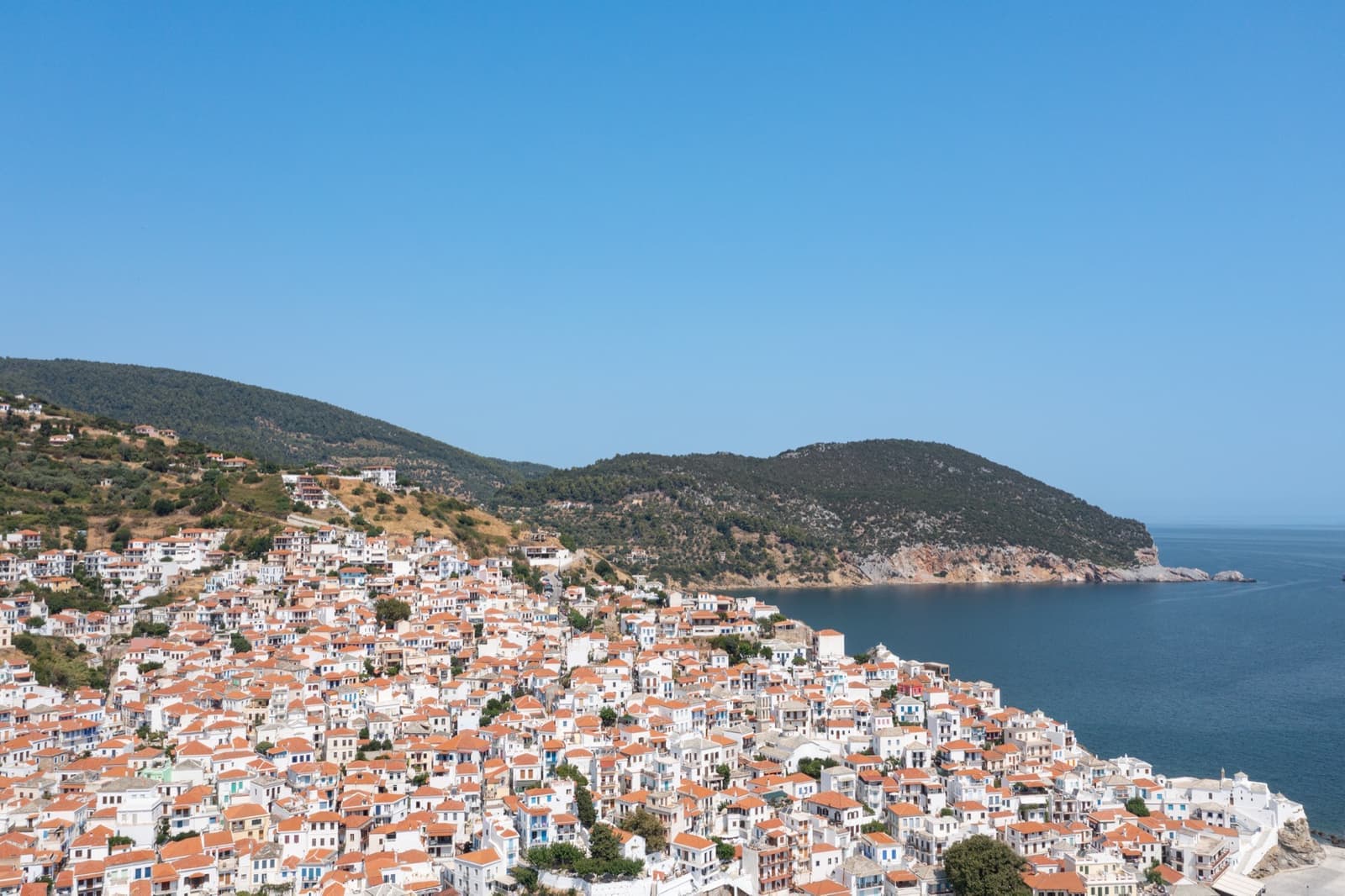 White houses with red roofs climbing a hillside above a blue bay