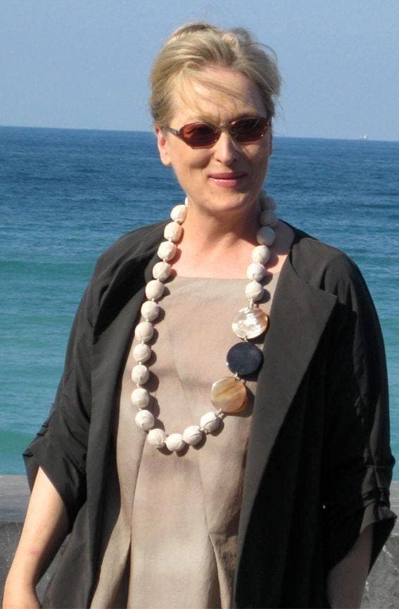 Meryl Streep in sunglasses and a long shell necklace, the sea behind her