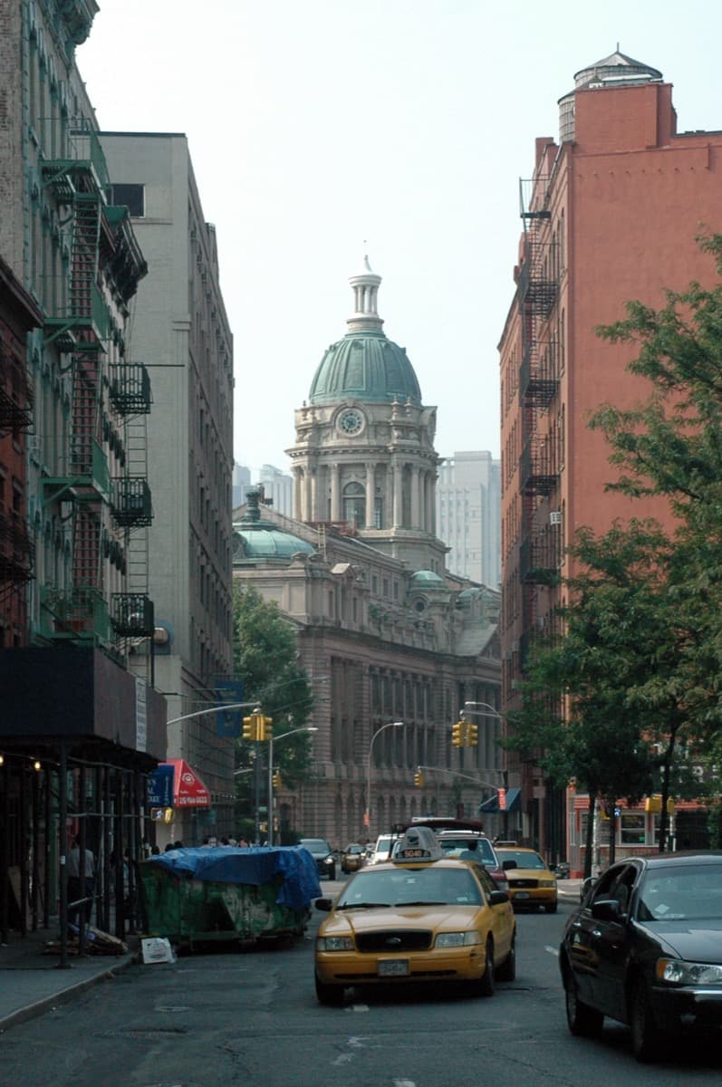 A short narrow street with tall old buildings and a domed tower at the end