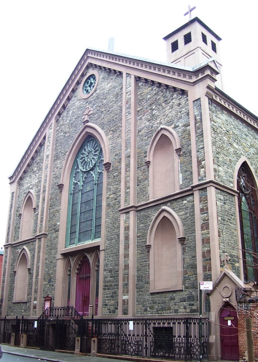 The pale stone front of a Gothic Revival church seen from the street