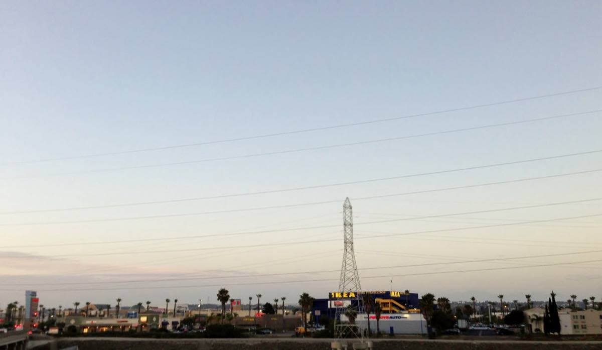 A flat horizon of low buildings and a tall electricity pylon at dusk