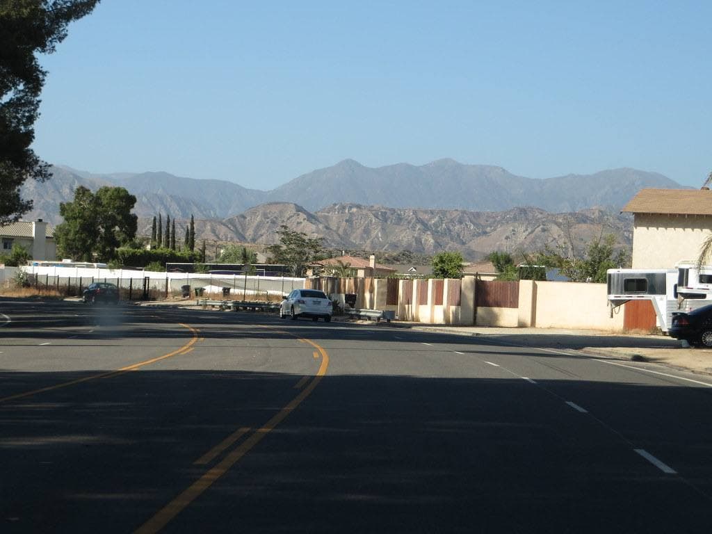 A wide suburban road with low walls and the San Gabriel Mountains behind