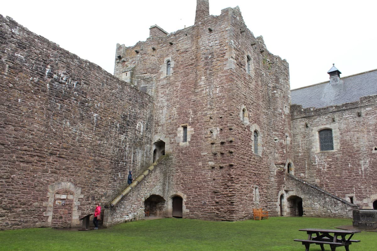 Doune Castle seen across its grounds, a grey stone gatehouse and keep under a pale sky.