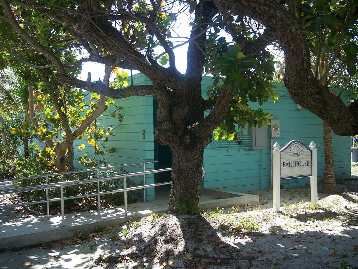 A teal-painted bathhouse with a sign, half hidden by a spreading tree