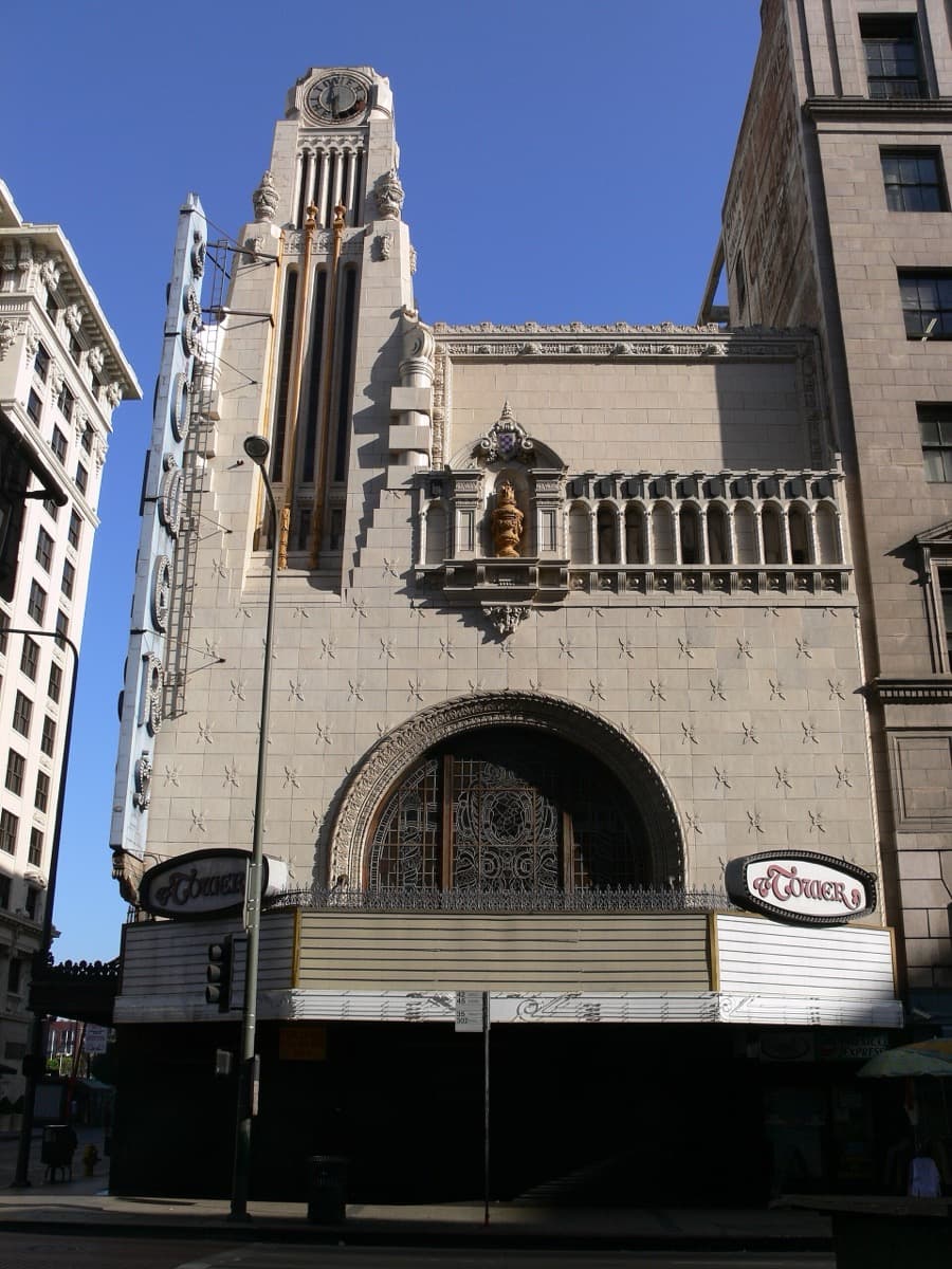 A cream terracotta cinema tower with a clock above a curved Broadway entrance