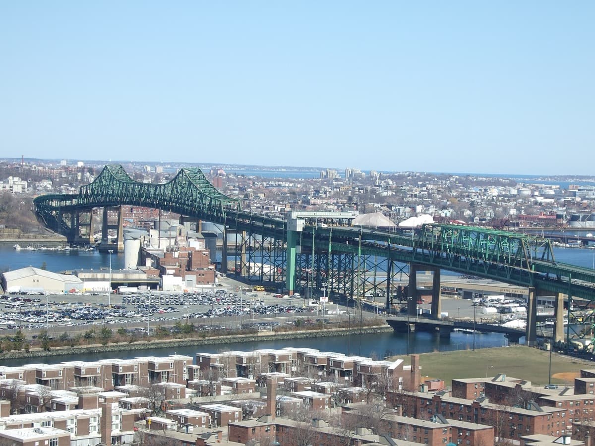 A long steel truss bridge crossing a river with a city skyline behind