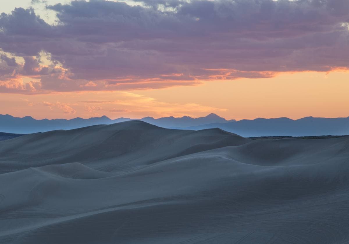 Smooth white sand dunes in blue shadow under an orange evening sky
