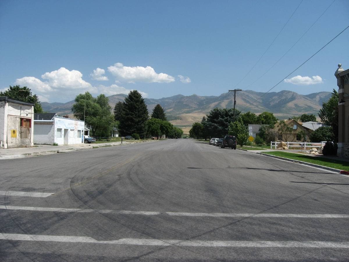 A wide quiet street in a small town with trees and mountains