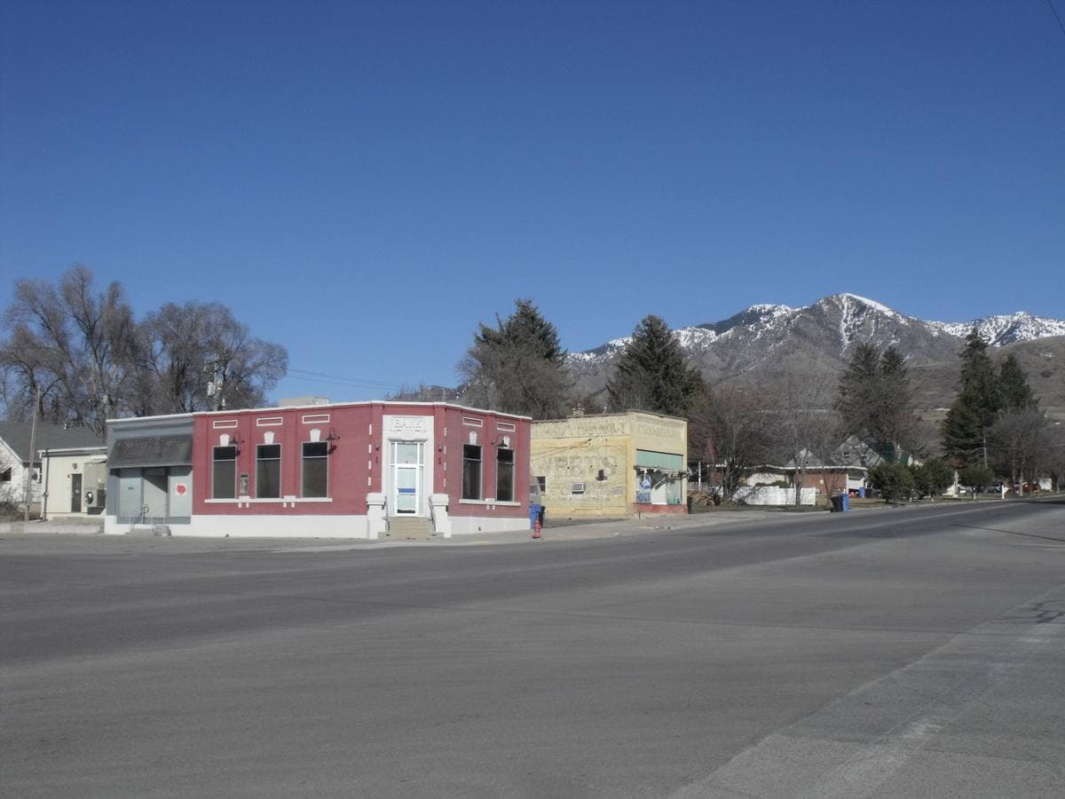 A small-town crossroads with a red brick bank and snowy mountains behind