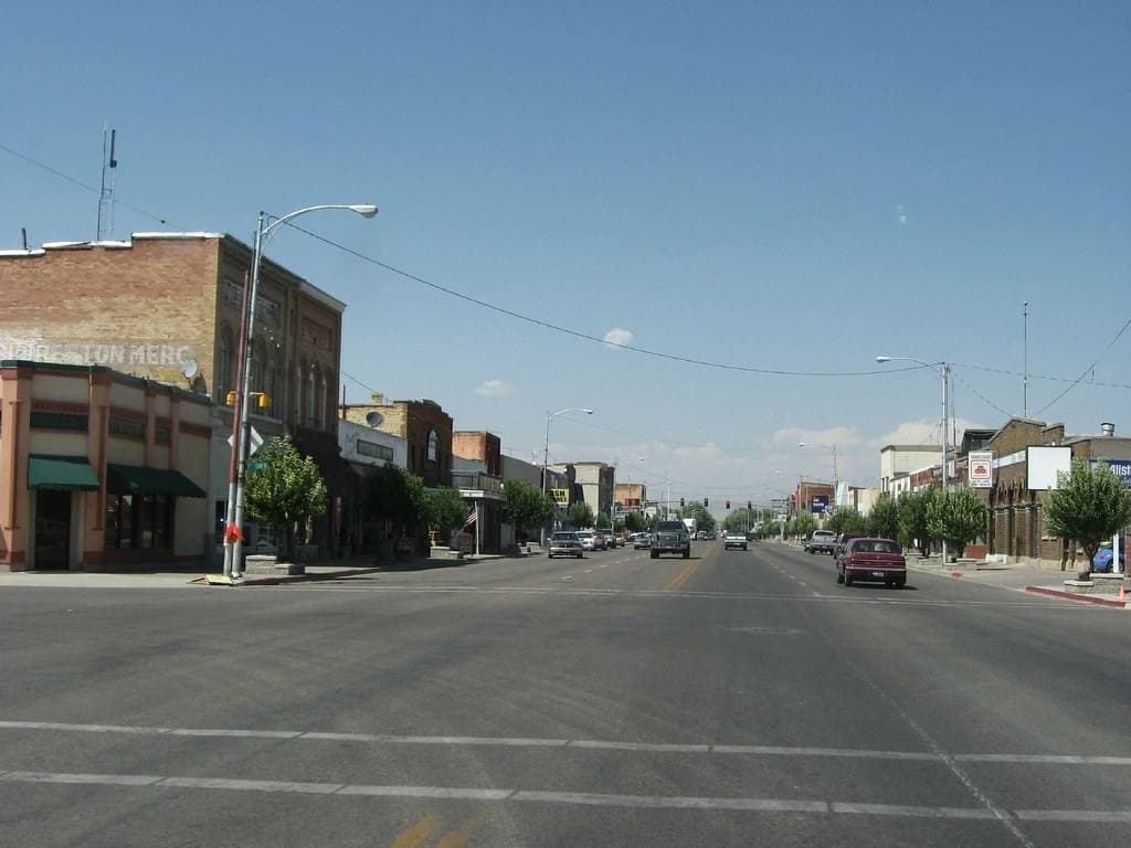 A wide main street of low brick shopfronts running towards hills