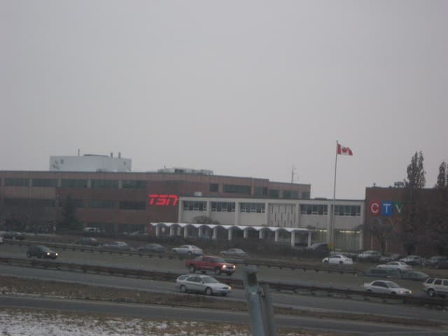 A low broadcast studio building beside a highway with a tower behind it