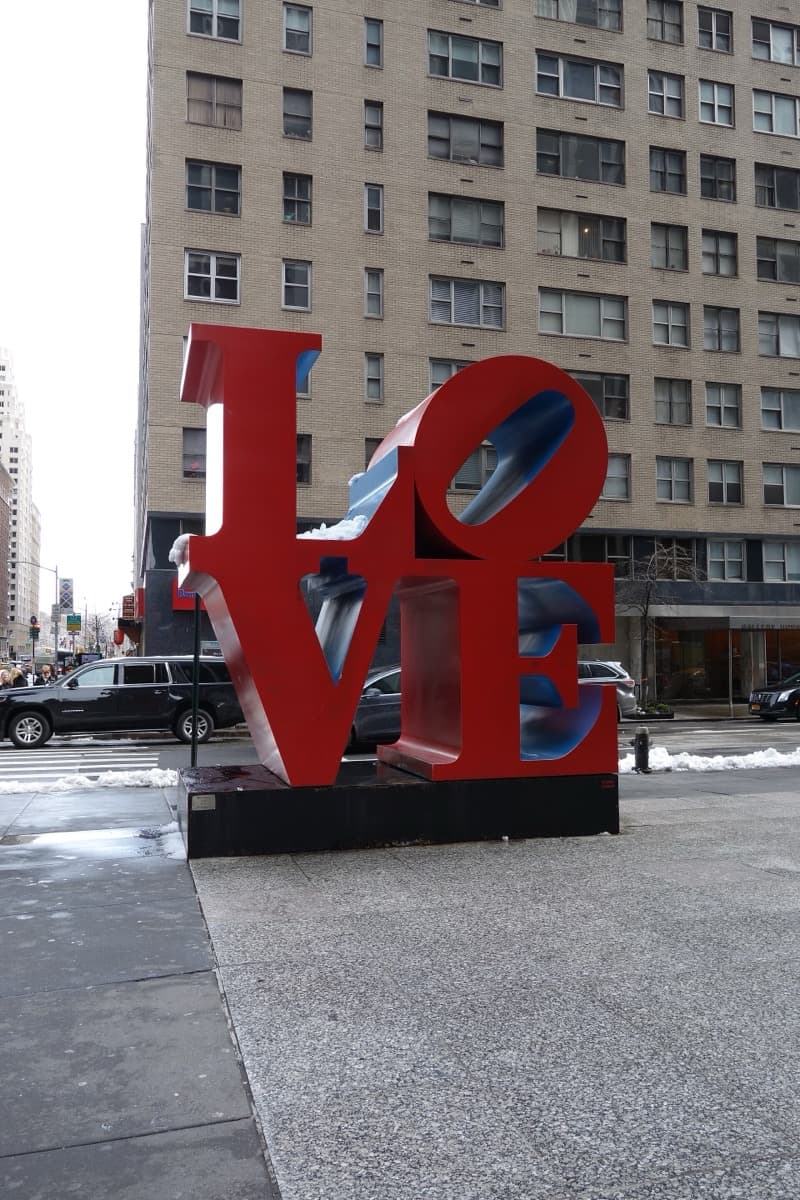 A red sculpture on a Manhattan pavement in front of a tall office tower