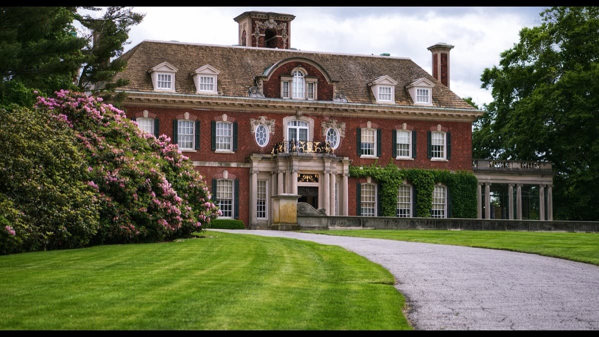 A large brick mansion behind a lawn under a cloudy sky