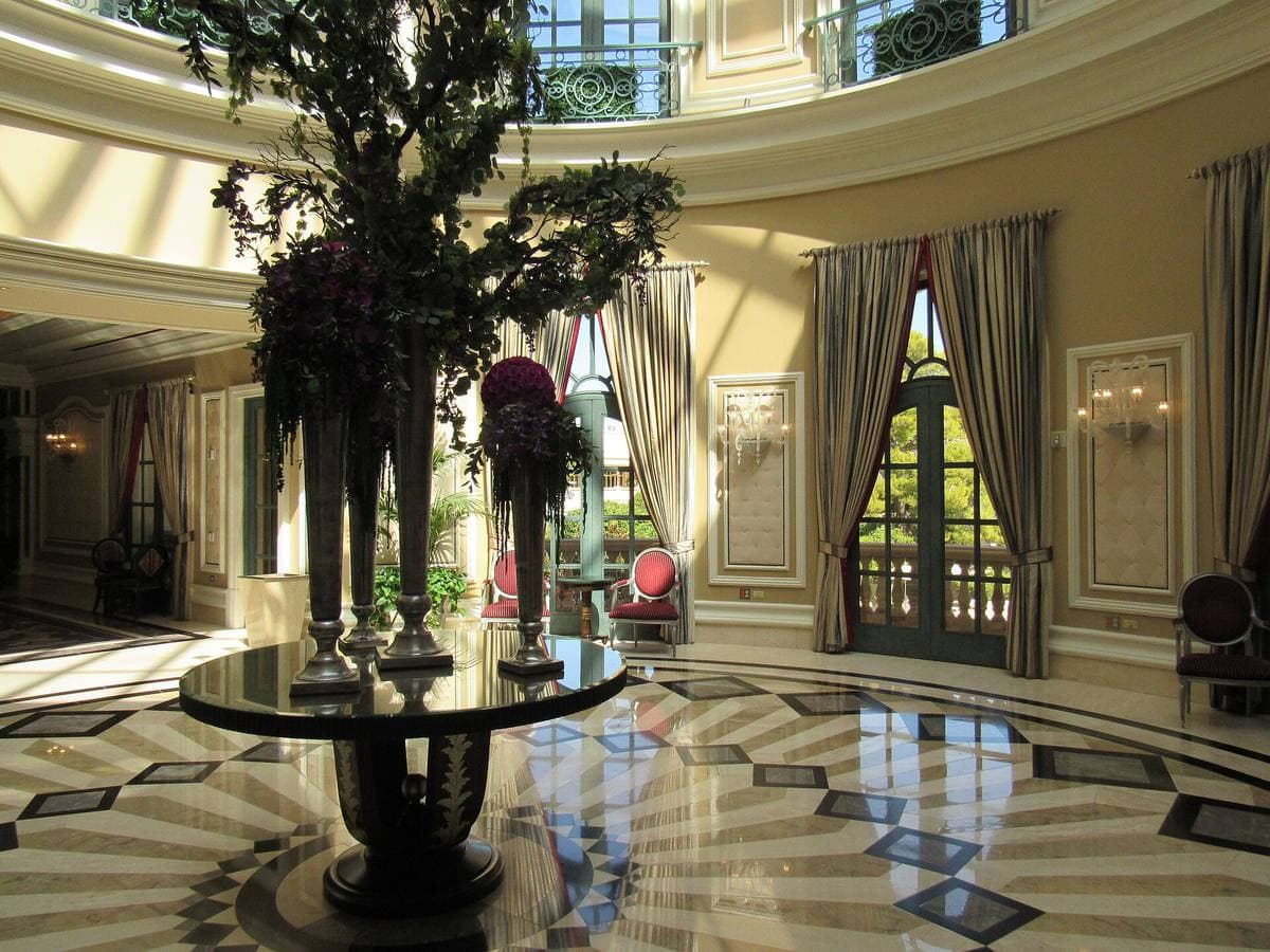 A marble rotunda with a round table, a tall flower arrangement and draped windows