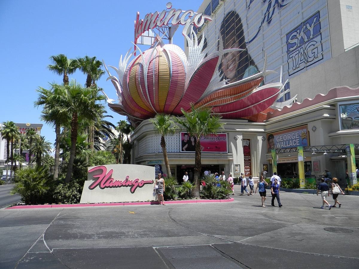 A pink and orange feather sculpture over a hotel entrance with palm trees