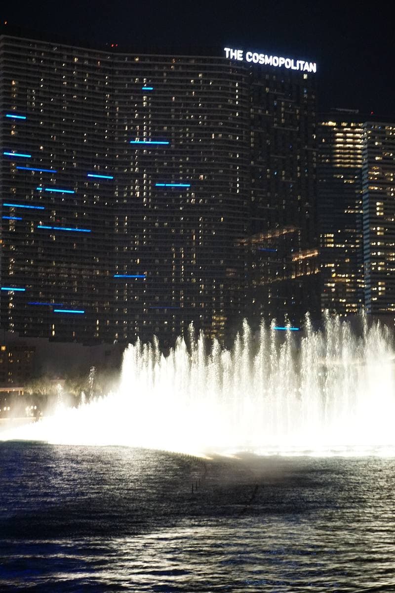 A row of lit water jets against a dark tower at night
