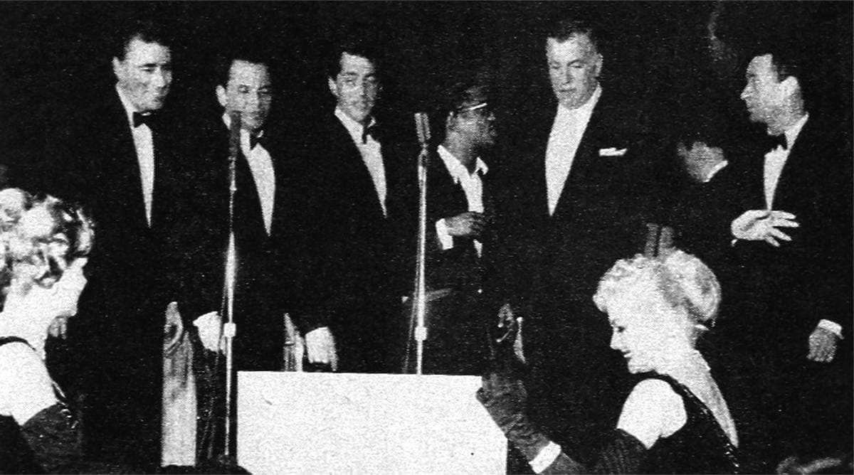 Six men in dinner jackets on a nightclub stage, black and white
