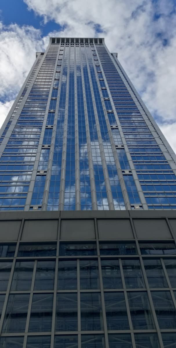 A tall glass office tower with a stepped top seen from street level
