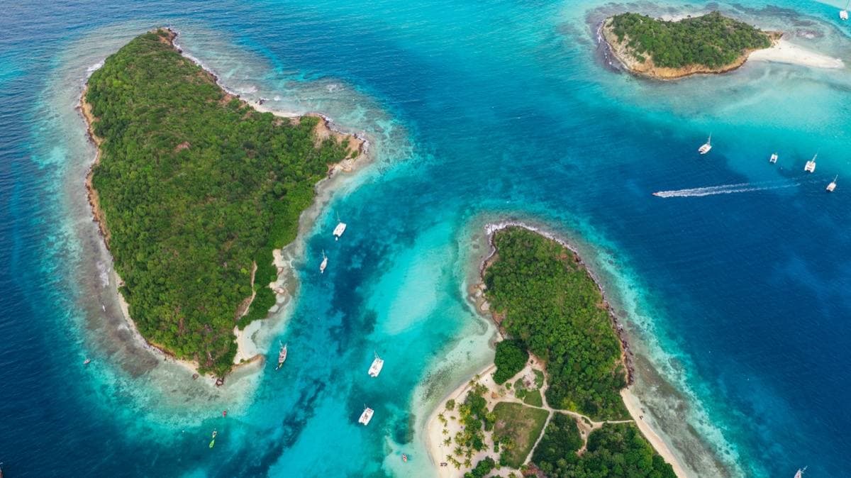 Aerial view of small wooded islands ringed with white sand in turquoise water, boats at anchor