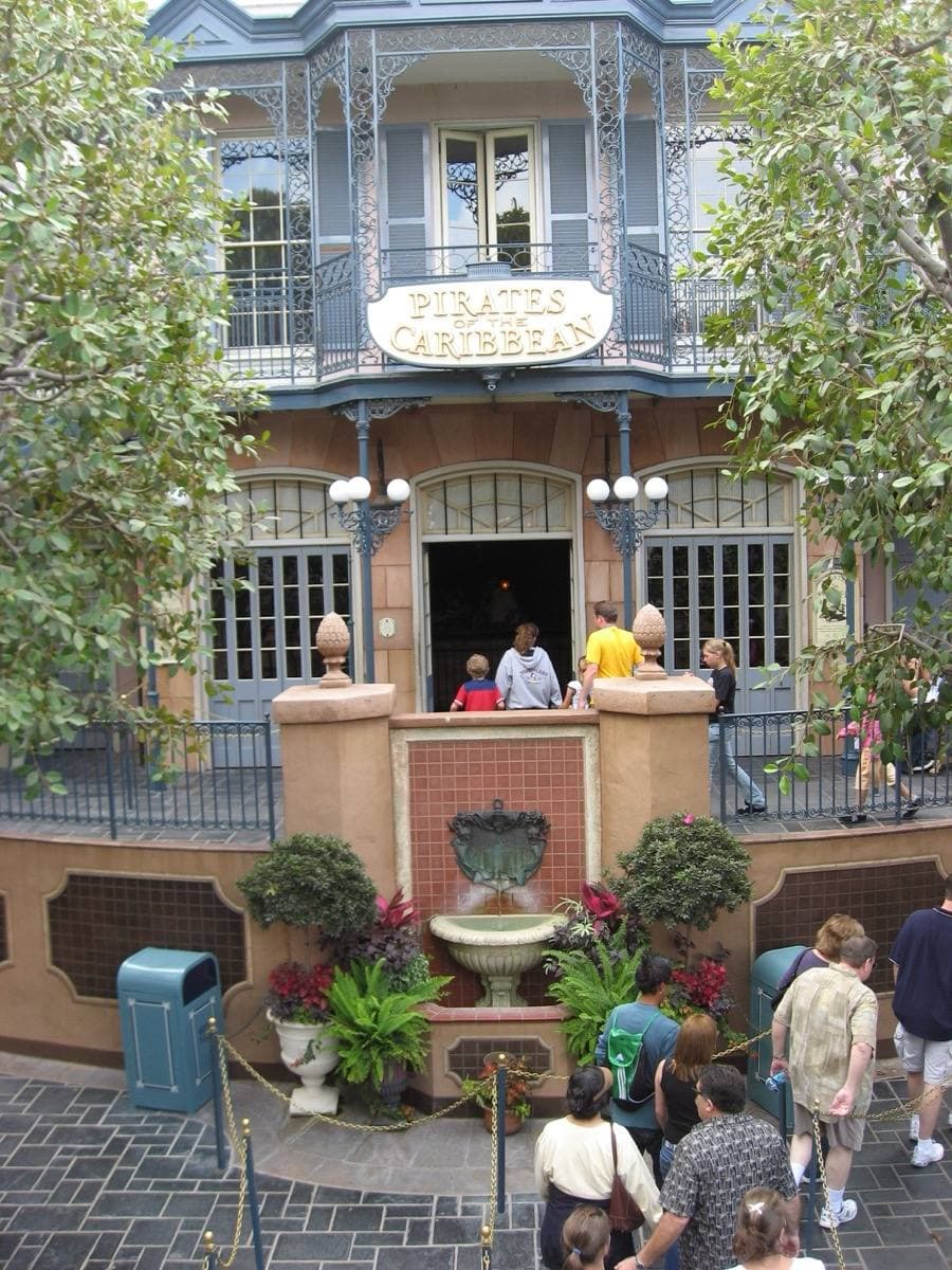 A pale blue New Orleans-style building with iron balconies and visitors at the ride entrance