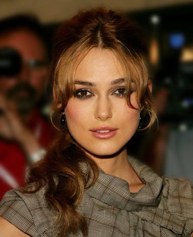 Keira Knightley with her hair pinned back, in a checked wool top, looking at the camera