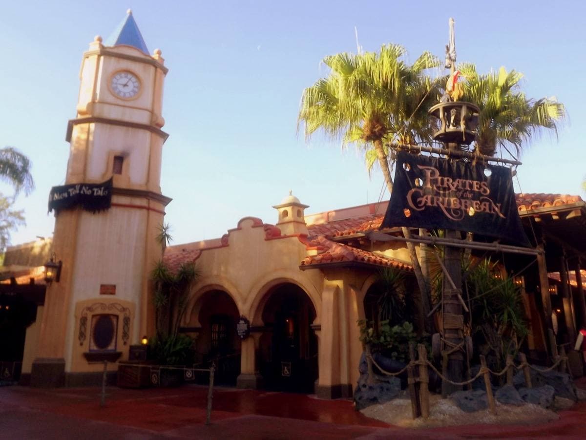A Spanish colonial clock tower and arcade with palm trees and a hanging banner