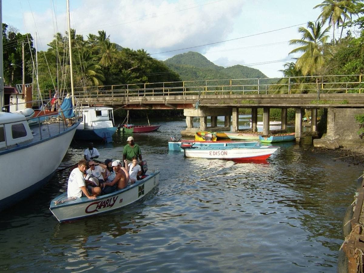 Small boats with passengers by a low bridge, green hills behind