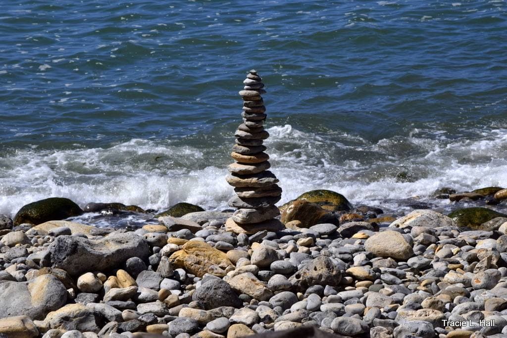 A cairn of stacked stones on a pebble beach with waves breaking behind