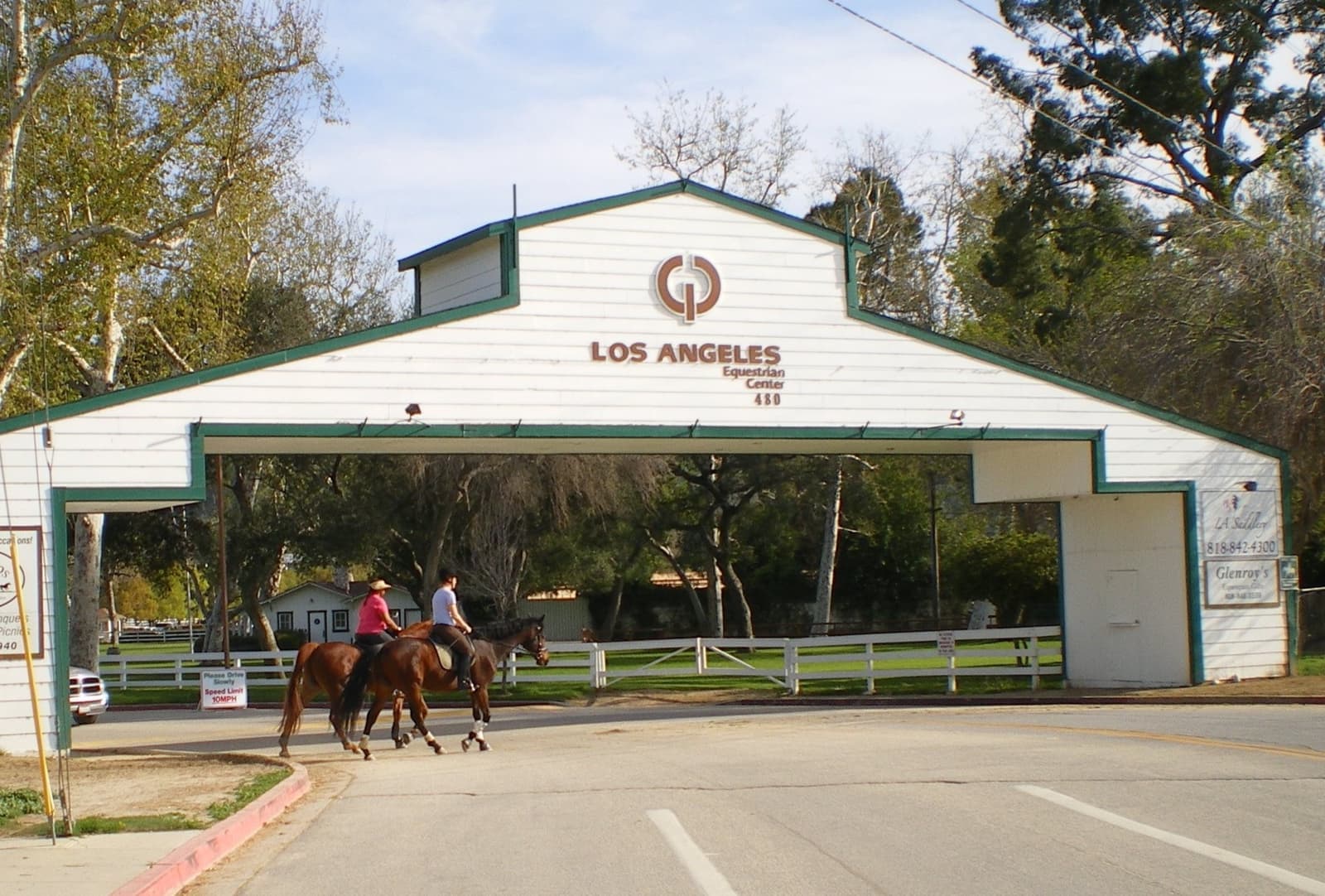 Riders on horseback passing under a white gatehouse sign