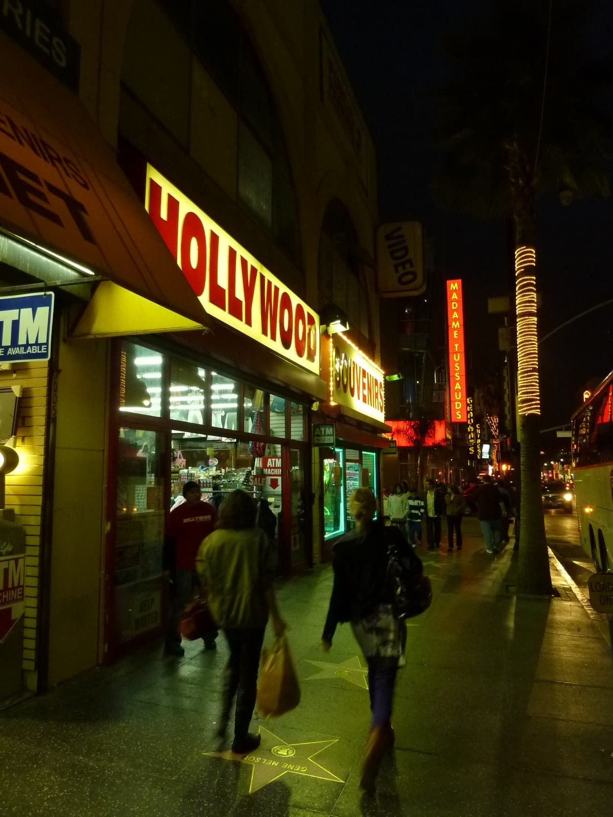 A bright souvenir shop sign on Hollywood Boulevard at night, with people walking past