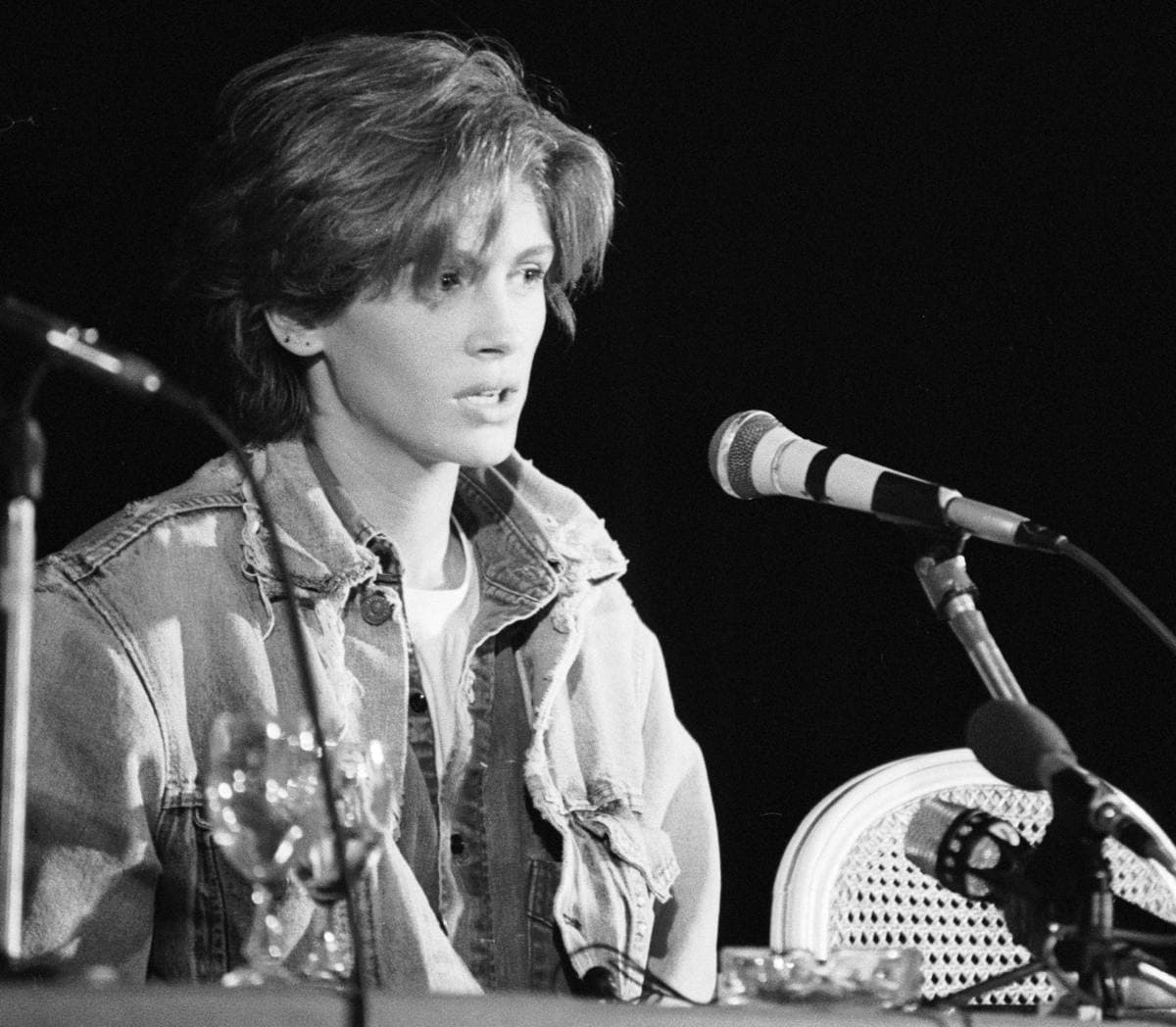 Black-and-white photo of Julia Roberts in a denim jacket at a table of microphones