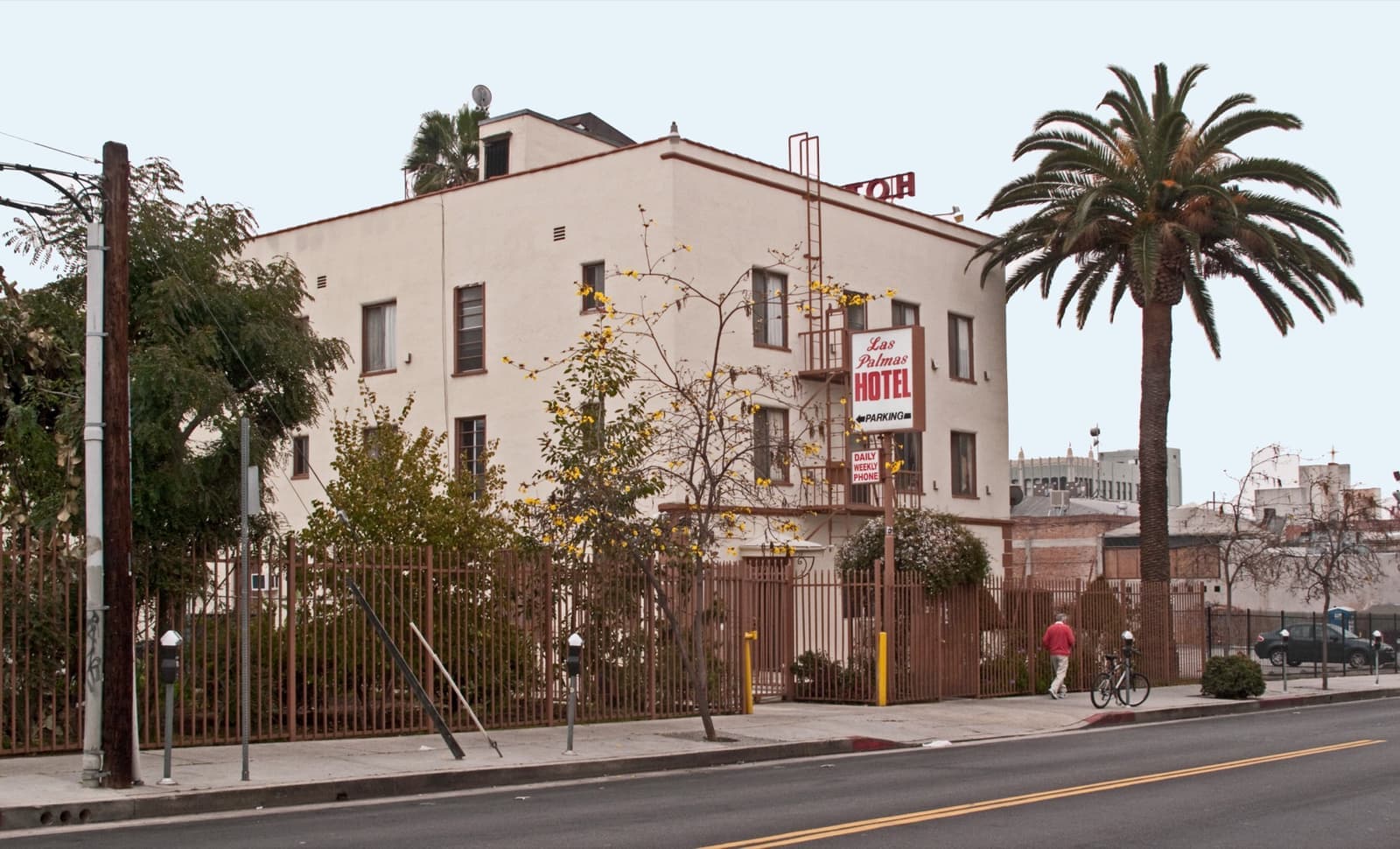 A pale three-storey building with a fire escape and a tall palm tree on the corner