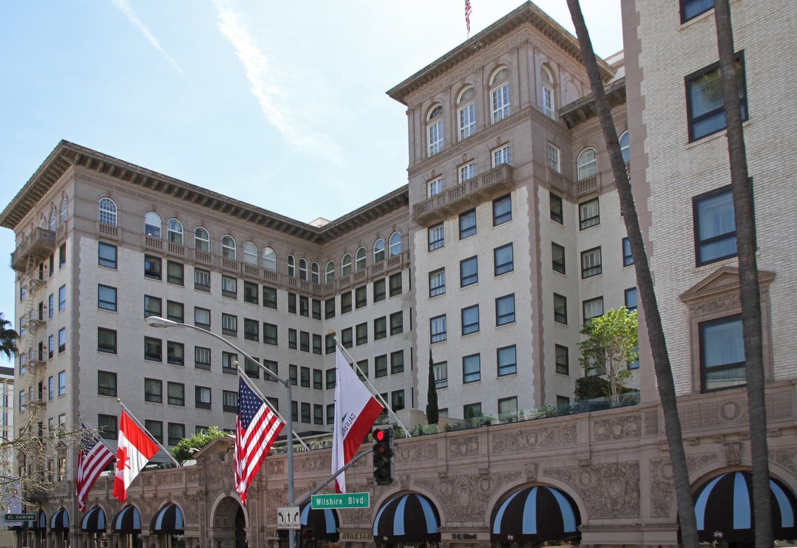 A tall cream hotel with striped black-and-white awnings and flags over the entrance