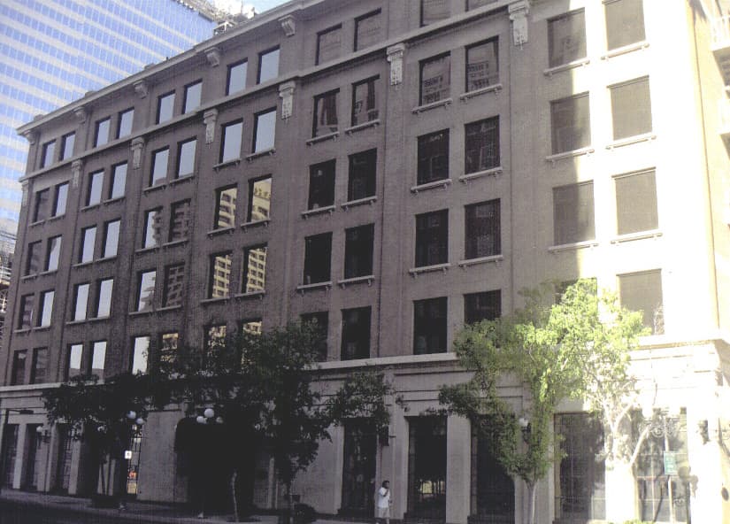 A six-storey brick and stone office building on a downtown street corner, with trees at street level